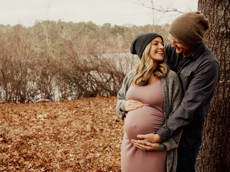 couple holding the belly of the woman who is pregnant in the middle of a field