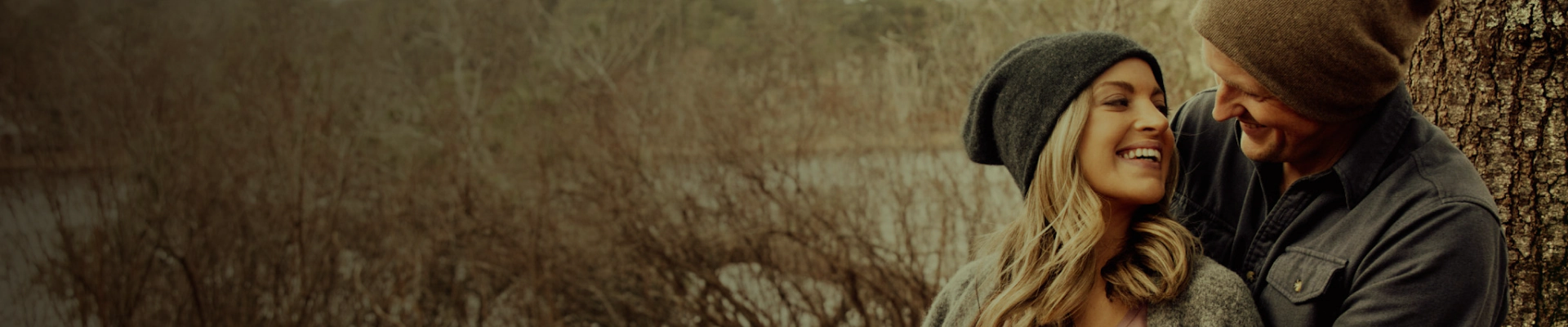 happy couple with beanies in the middle of a field with leafless trees