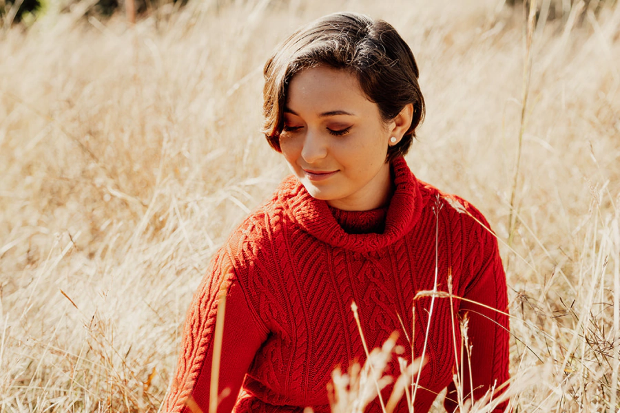 woman with dark brown short hair and a red sweater in the middle of a field