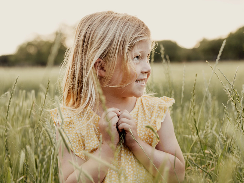 blonde girl with a yellow dress on the middle of a field with some trees at the back