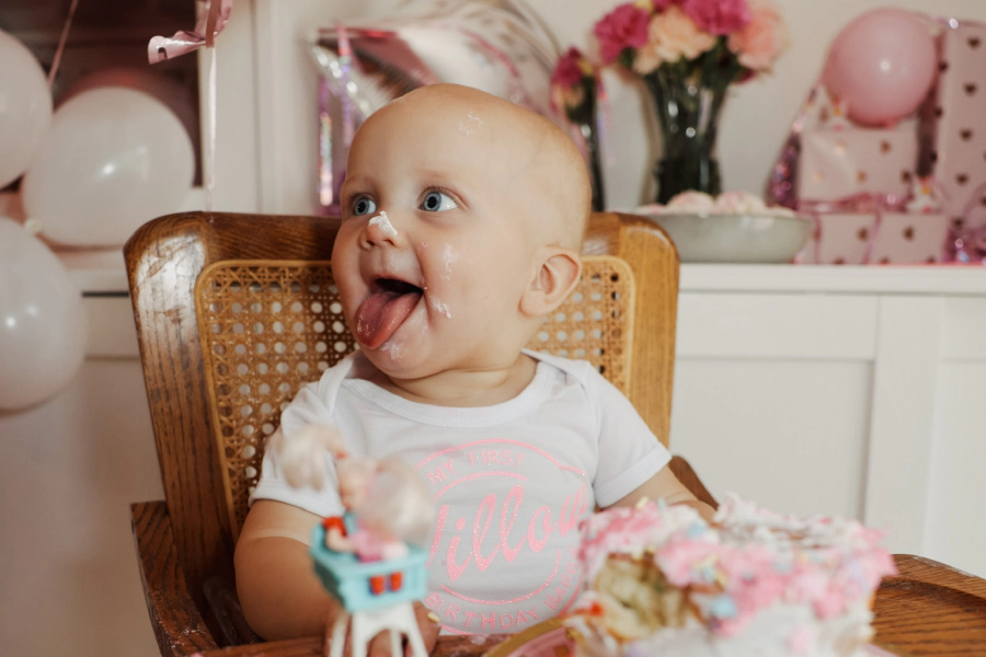 child with a small cake in front and some balloons around it
